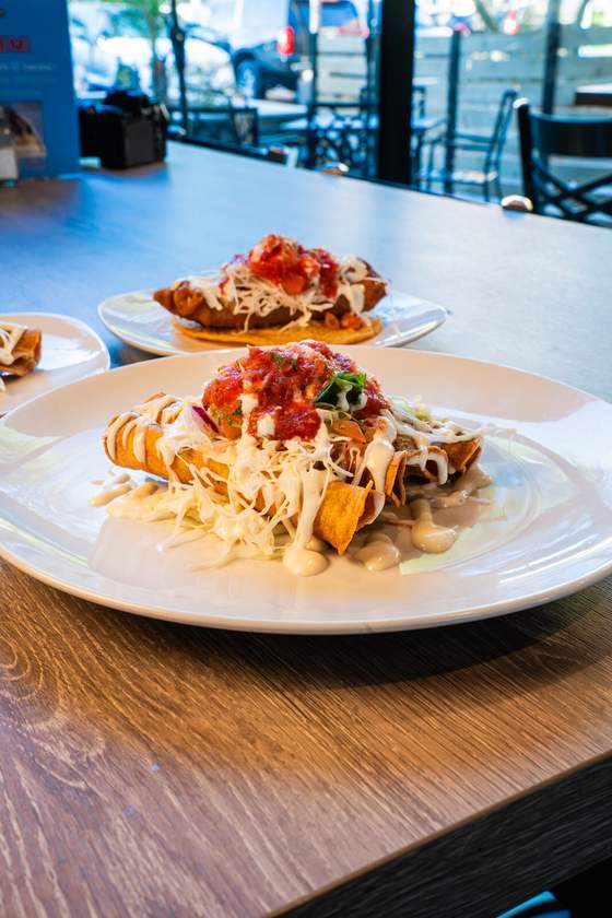 Two plates of shrimp flautas topped with crema and salsa on a patio table