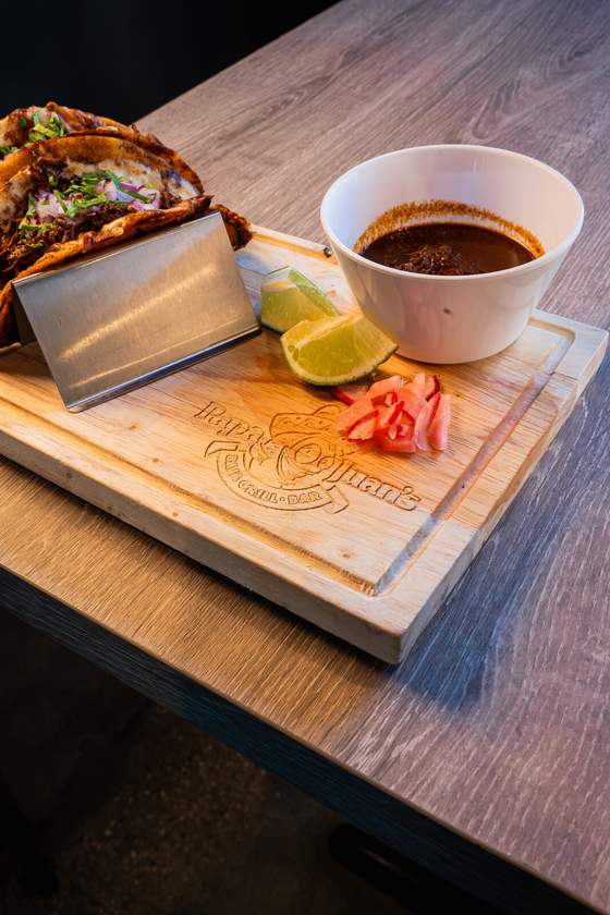 Quesabirria tacos on a wooden board with a bowl of consomme and lime