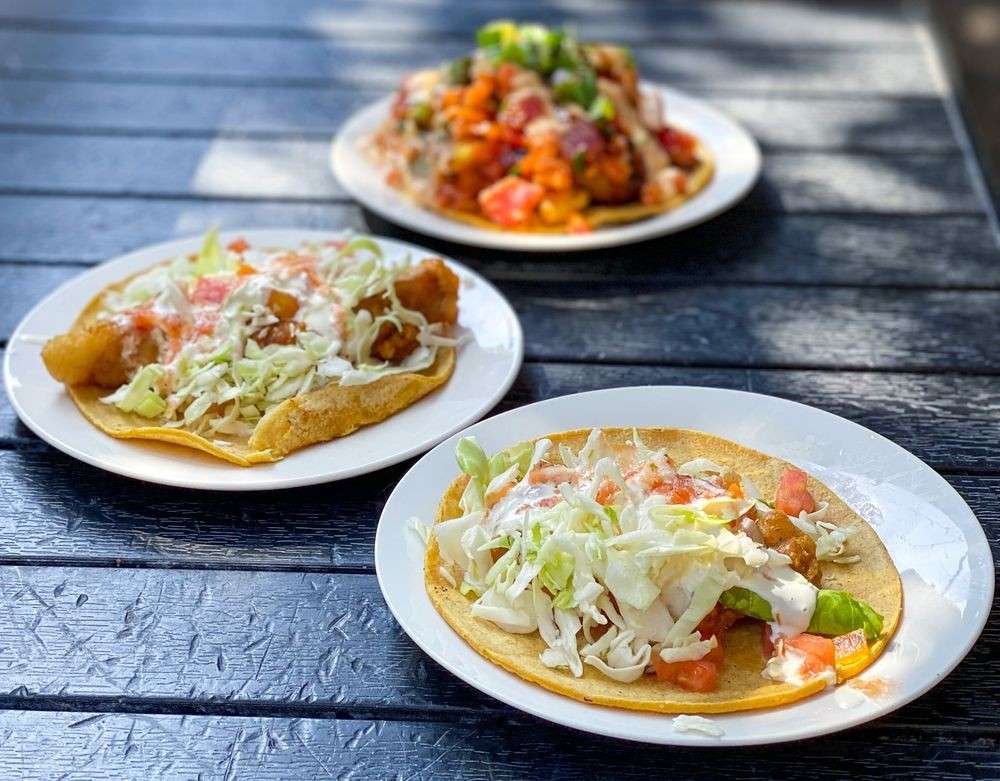 Three Baja tostadas on white plates on a patio table